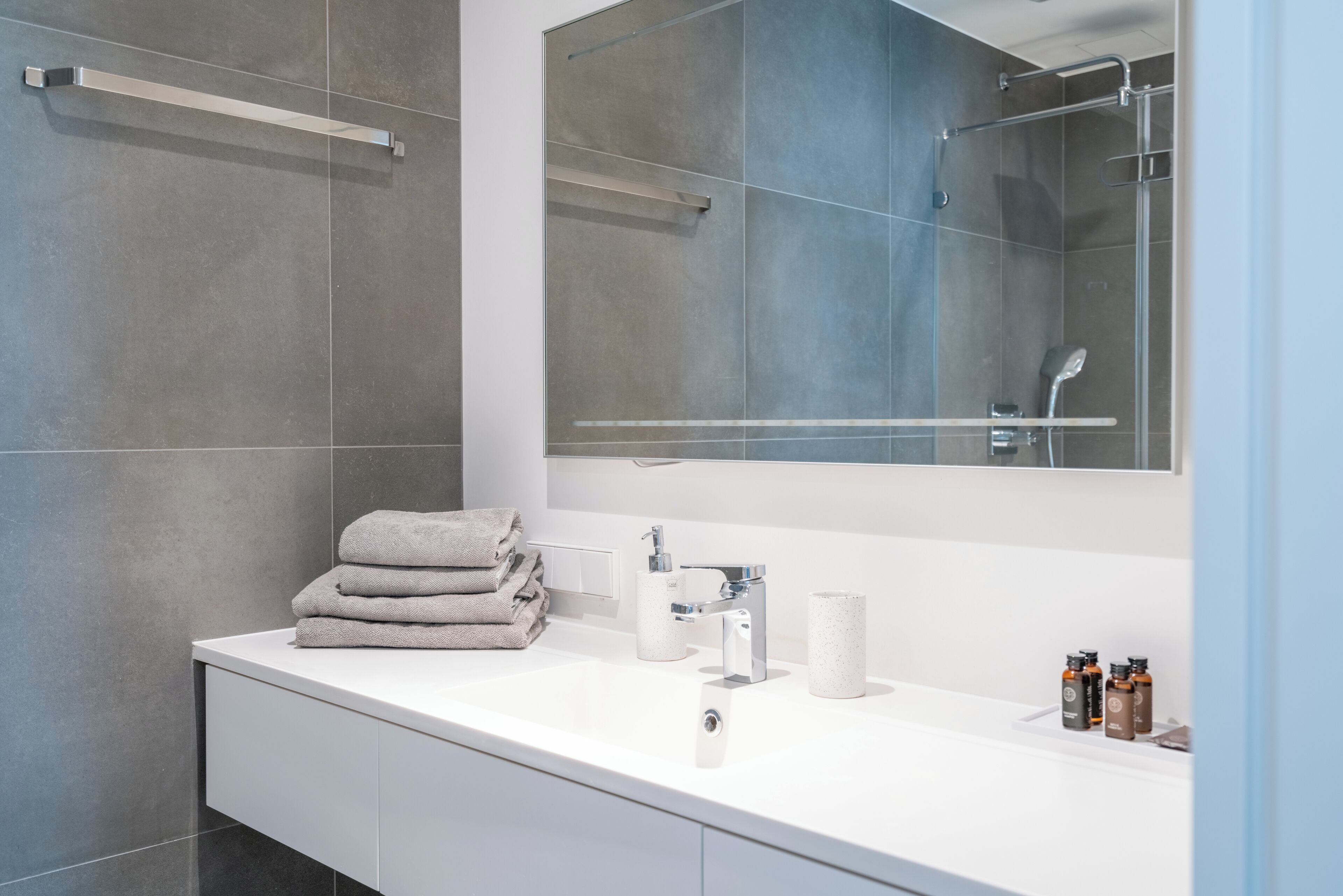Un baño moderno con un tocador blanco, un espejo grande y un box de ducha de vidrio.