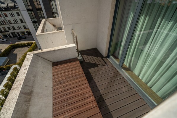 Un balcon doté d’un plancher en bois, d’un mur en béton et d’une porte en verre.