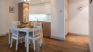 A modern dining area with a white table and chairs, a wooden accent wall, and a pendant light. - Easyrooms Dzirnavu (Riga)