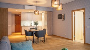 A modern living room with a sofa, dining table, and chairs. There is a kitchen area with cabinets and a refrigerator. - Easyrooms Dzirnavu (Riga)
