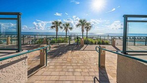 A paved walkway leading to a beach with palm trees, a clear sky, and the sun shining. - 1105 Dimucci Twin Towers (Daytona Beach Shores)