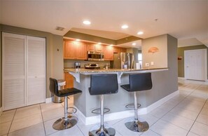 A modern kitchen with a central island, three bar stools, and stainless steel appliances.