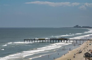 A beach with a pier extending into the ocean, a sandy shore, and a distant city skyline.