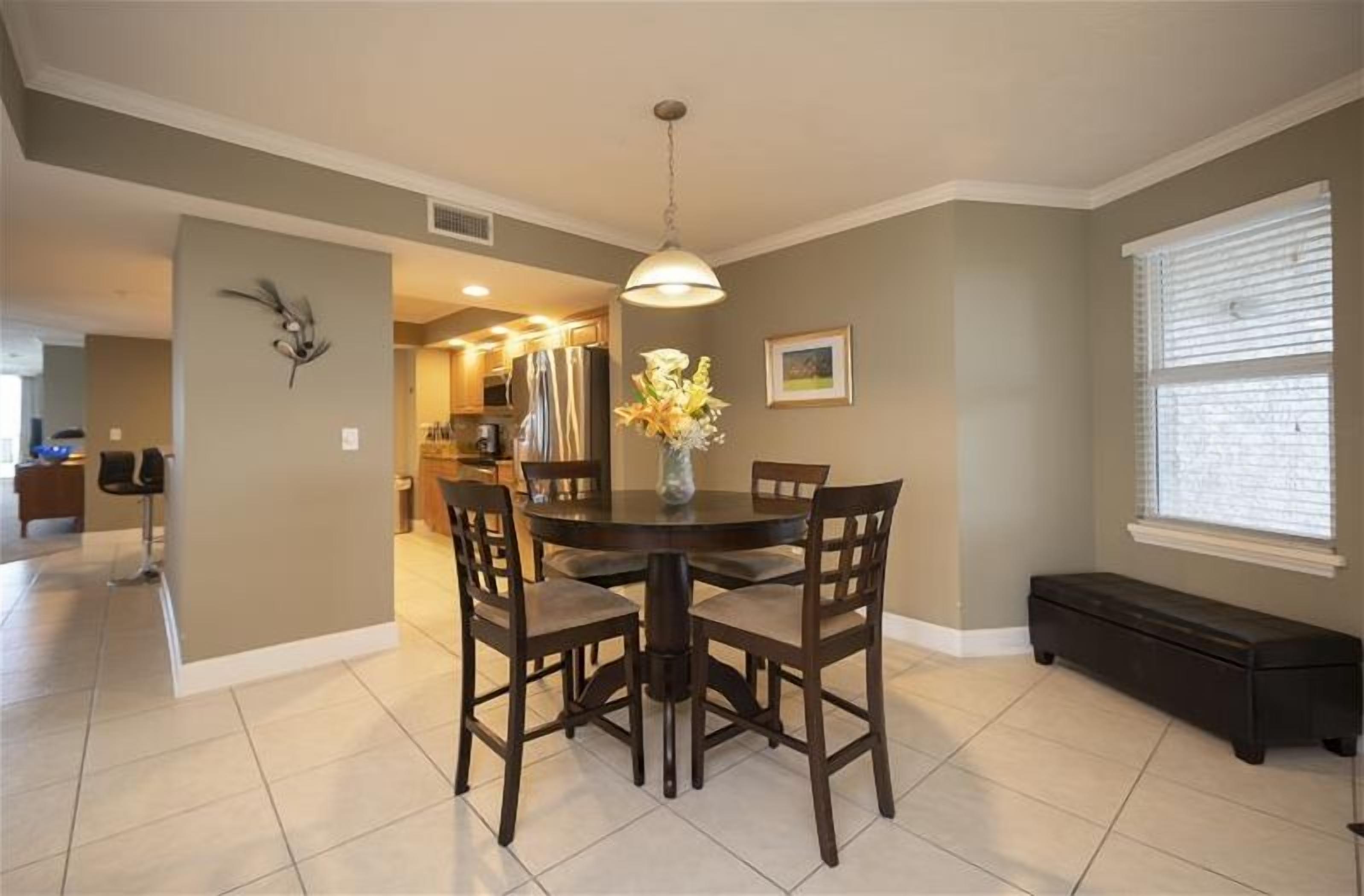 A dining area with a round table, four chairs, and a vase with flowers.