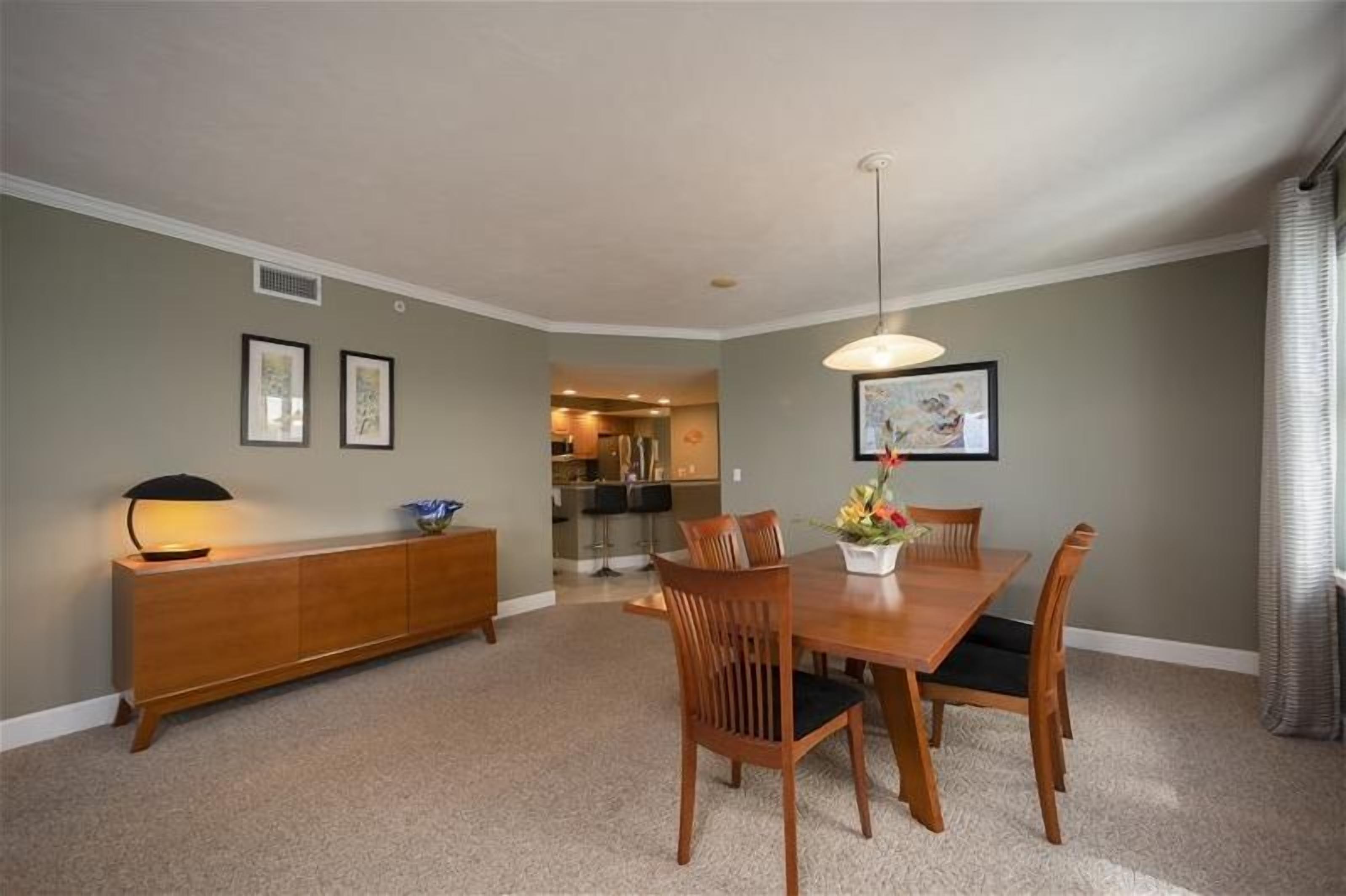 A dining room with a wooden table and chairs, a sideboard, and framed artwork on the walls.
