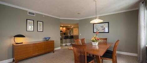 A dining room with a wooden table and chairs, a sideboard, and framed artwork on the walls.