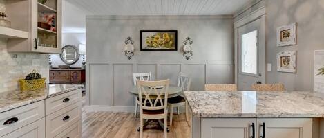 A kitchen with a wooden floor, white cabinets, a marble countertop, and a dining area with a table and chairs.