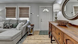 A living room with a grey sofa, a wooden dresser, a round mirror, and a door with a window above it. - A Southern Retreat / Cozy Getaway in the heart of Atlanta Sleeps 4 (Atlanta)