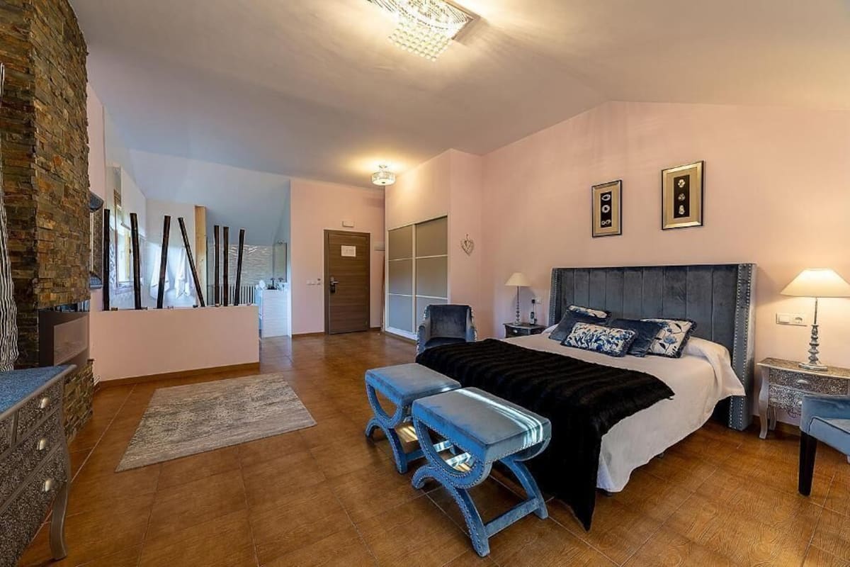 A bedroom with a bed, bench, bedside tables, and a brick wall.