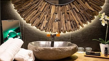 Un baño con un lavabo de piedra, decoración de pared de madera, un espejo, una toalla y una pequeña planta en maceta.