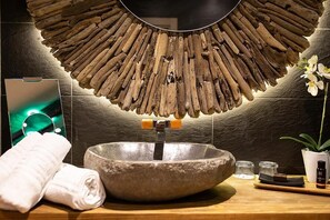 Un baño con un lavabo de piedra, decoración de pared de madera, un espejo, una toalla y una pequeña planta en maceta.