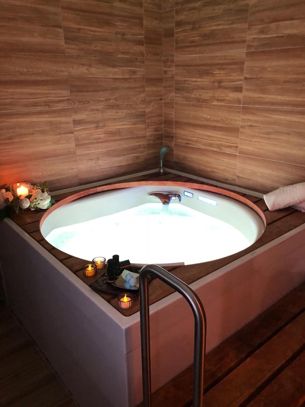 Un baño moderno con una bañera independiente, paredes de madera y una mesita auxiliar con velas.