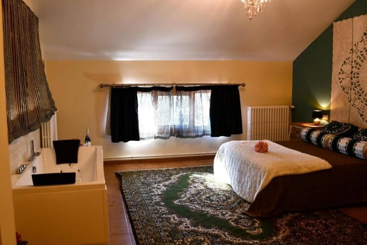 A bedroom with a bed, a window with curtains, a radiator, a sink, and a chandelier.