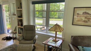 Ein Wohnzimmer mit einem Relaxsessel, einem braunen Ledersofa, einem Couchtisch mit Lampe und einem Bücherregal.