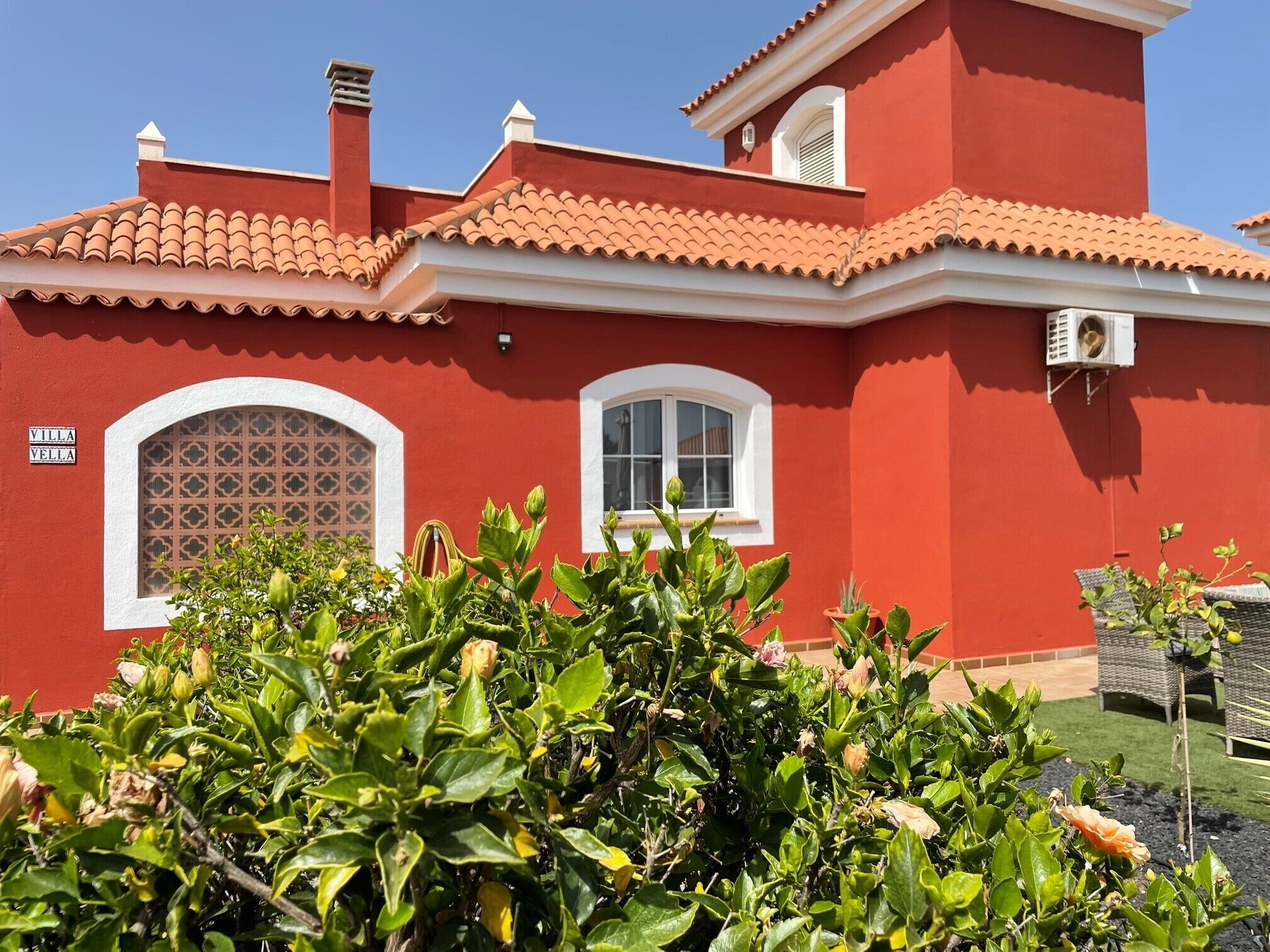 Eine rote Villa mit Ziegeldach, zwei Fenster mit weißen Rahmen und ein Schild mit der Aufschrift 'VILLA VELLA'.