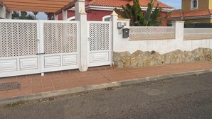 Un conjunto residencial con acceso restringido, una casa de techo rojo, un muro de piedra y una cerca blanca.