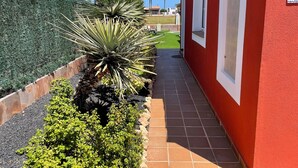 Un sendero conduce a un edificio rojo con arcos blancos, rodeado de setos cuidados y una diversidad de plantas.