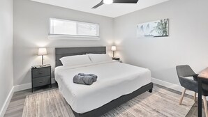 A modern bedroom with a bed, bedside tables, a desk, a chair, a ceiling fan, a window, and a wall art piece. - Ridgefield Estate, 5BED, Backyard, Games (Plano)