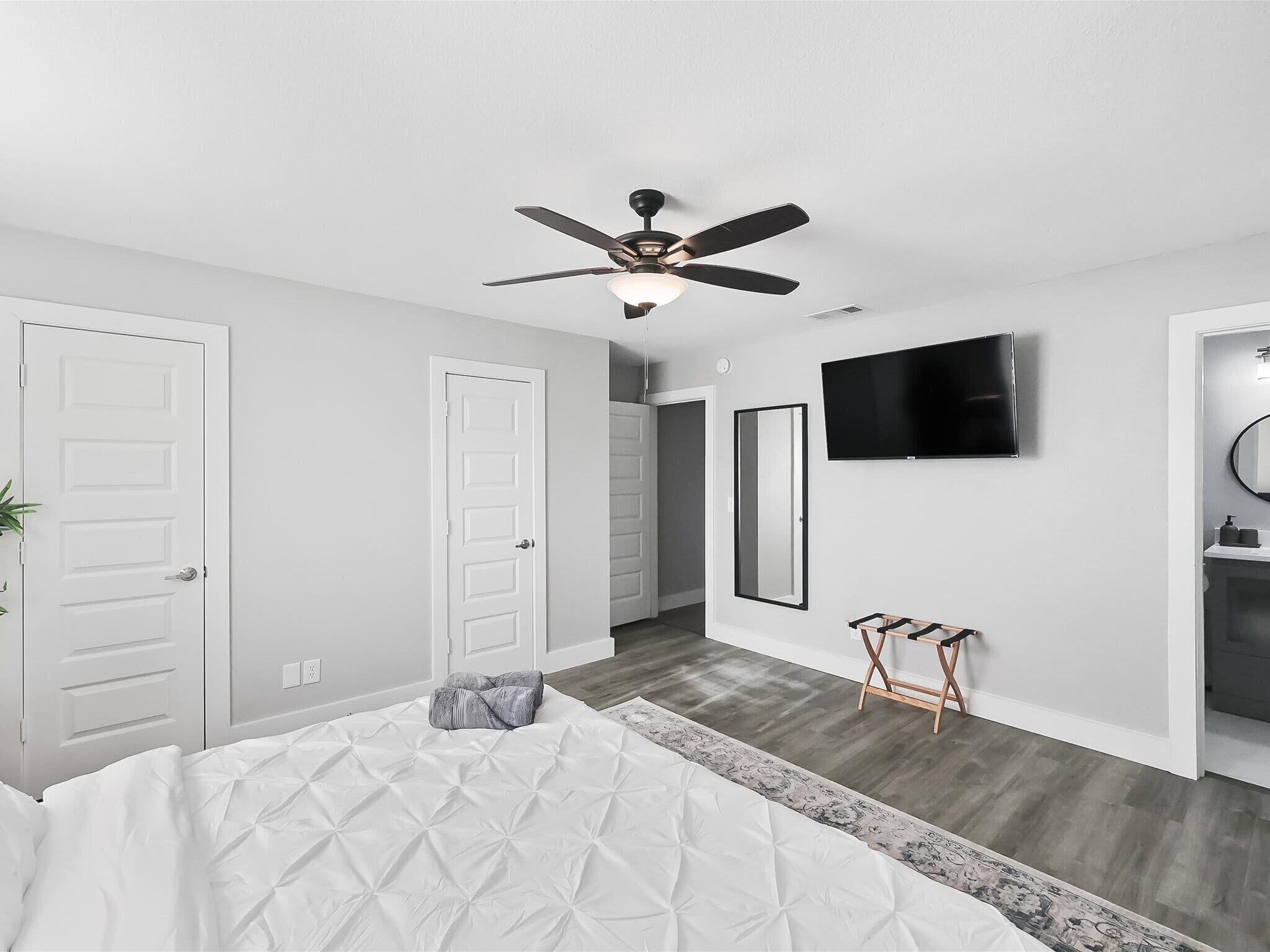 A bedroom with a bed, a ceiling fan, a TV, and a bathroom with a mirror.