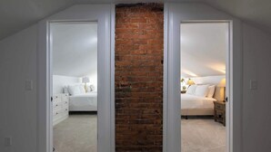 A bedroom with a brick wall, white bedding, and a nightstand with a lamp. - Two Condos for 14 Guests, 5 Bedrooms, Free Parking (Covington)