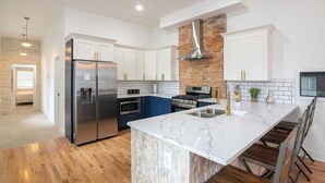 A modern kitchen with white cabinets, a stainless steel refrigerator, a brick wall, and a marble countertop. - Two Condos for 14 Guests, 5 Bedrooms, Free Parking (Covington)