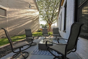 A patio with four chairs and a table, a brick wall, and a tree in the background.