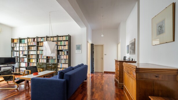 Un salón amplio con sofá azul, suelo de madera, una estantería y un televisor.