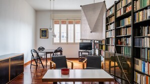 Una sala de estar moderna con piso de madera, una mesa de comedor con sillas, una estantería y un televisor.