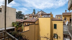 Una zona residencial con edificios amarillos, un balcón con barandilla de metal y un cielo despejado con nubes.