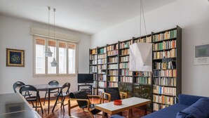 Una sala moderna con un sofá azul, una mesa de comedor con sillas y una amplia estantería llena de libros.