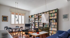 En moderne stue med en blå sofa, et spisebord med stole og et stort bogreol fyldt med bøger.