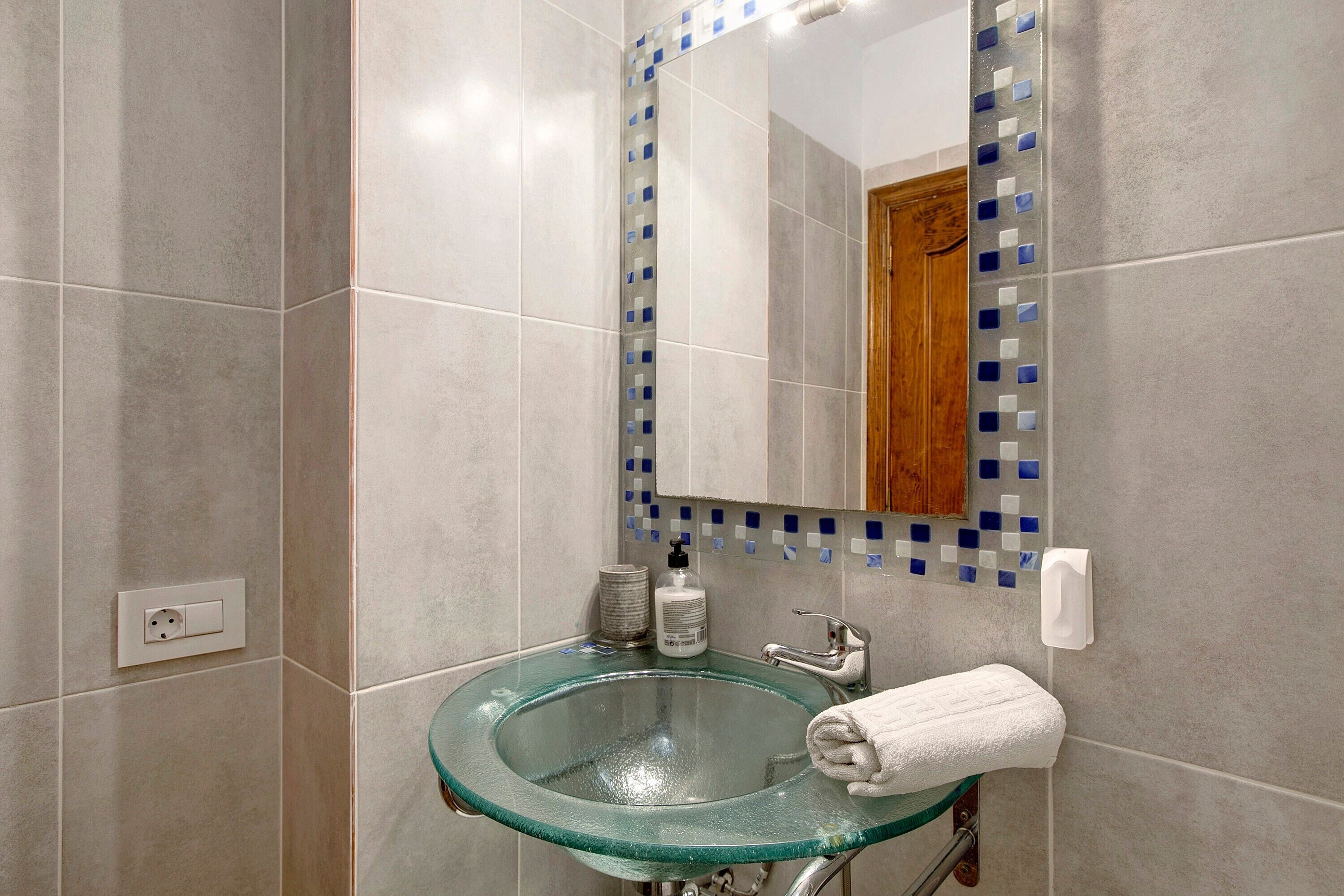 A bathroom with a glass sink, a mirror, and a towel rack.
