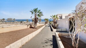 Une promenade en bord de mer bordée de palmiers et un bâtiment doté d’un toit plat, qui mène à la plage.