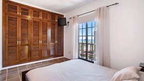 Une chambre à coucher avec un grand lit, une armoire en bois, une télévision et une fenêtre donnant sur un beau paysage.