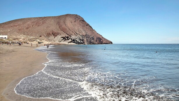 Une plage avec une grande colline en arrière-plan, un ciel dégagé et une eau calme.