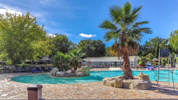 A pool area with lounge chairs, palm trees, and a clear blue sky.
