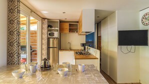 A compact kitchen with a microwave, stove, and cabinets, a dining area with a table set for four, and a TV mounted on the wall.