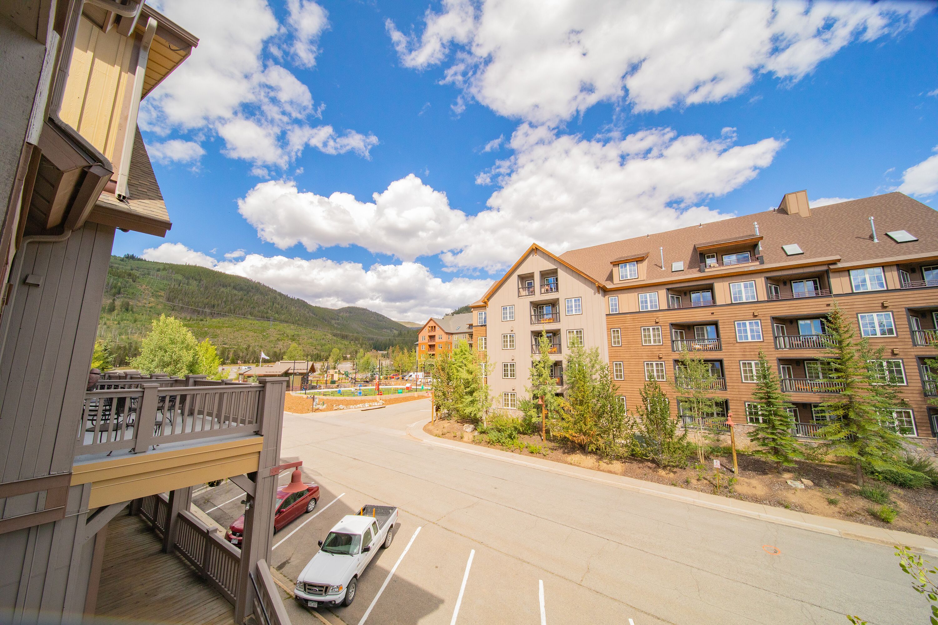 A multi-story hotel with balconies, a parking lot, and a mountainous backdrop.