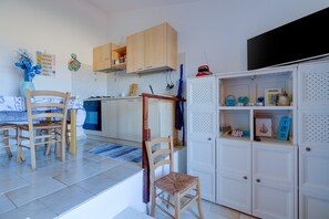 A kitchen with wooden cabinets, a dining table with chairs, a white cabinet with shelves, and a blue vase on the wall.