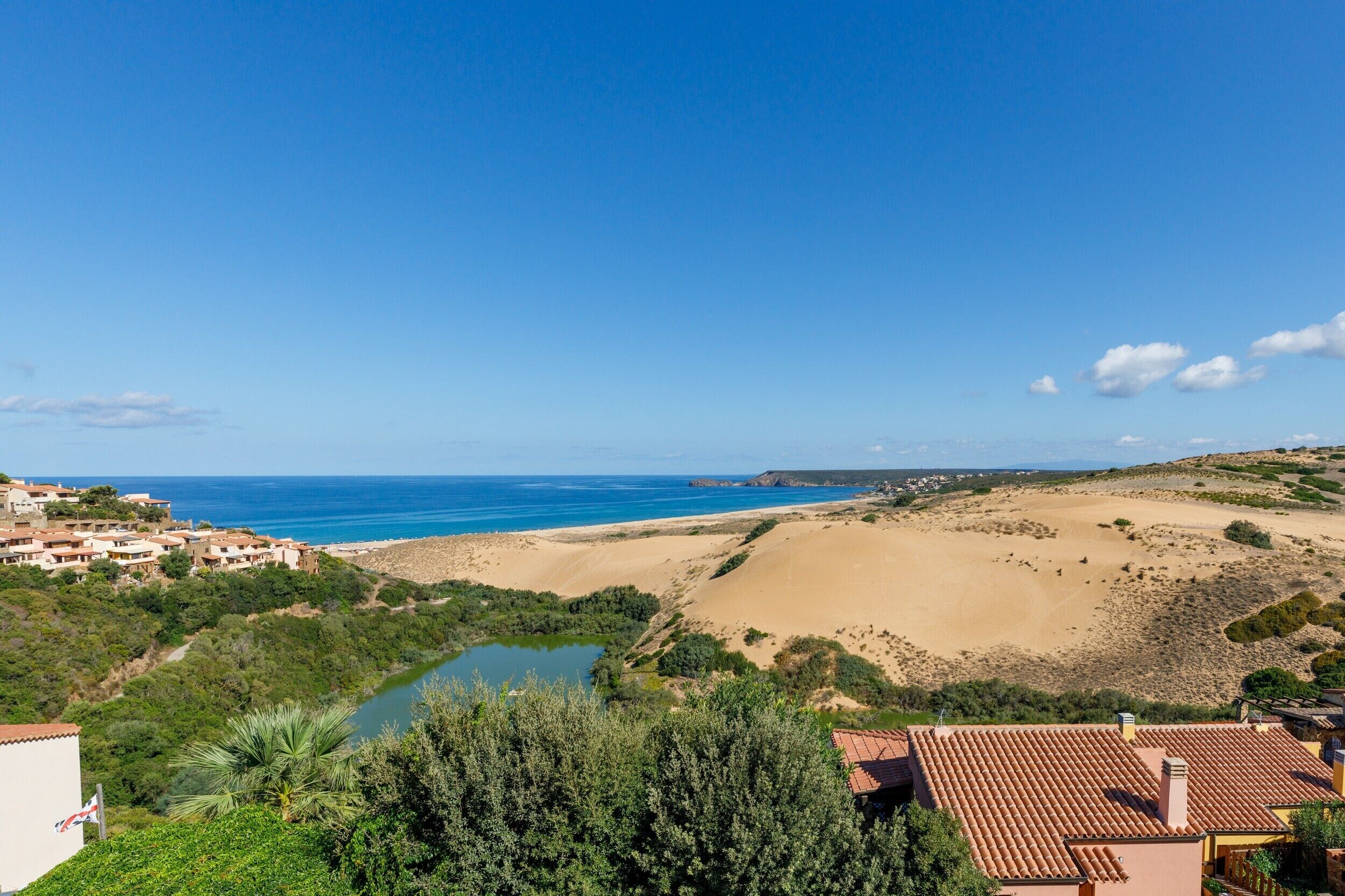 A coastal landscape with a beach, dunes, and a small body of water.