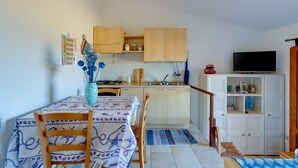 A compact kitchen with wooden cabinets, a dining table with chairs, a TV, and a small TV stand with items.