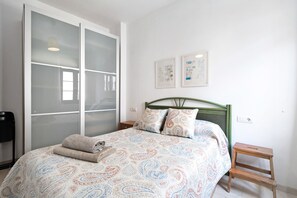 Een slaapkamer met een bed, een groen hoofdeinde, een nachtkastje, een houten kruk en een schuifdeur met glas.