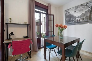 Een eethoek met een tafel, stoelen, een vaas met bloemen, een bureau met stoel en een raam met gordijnen.