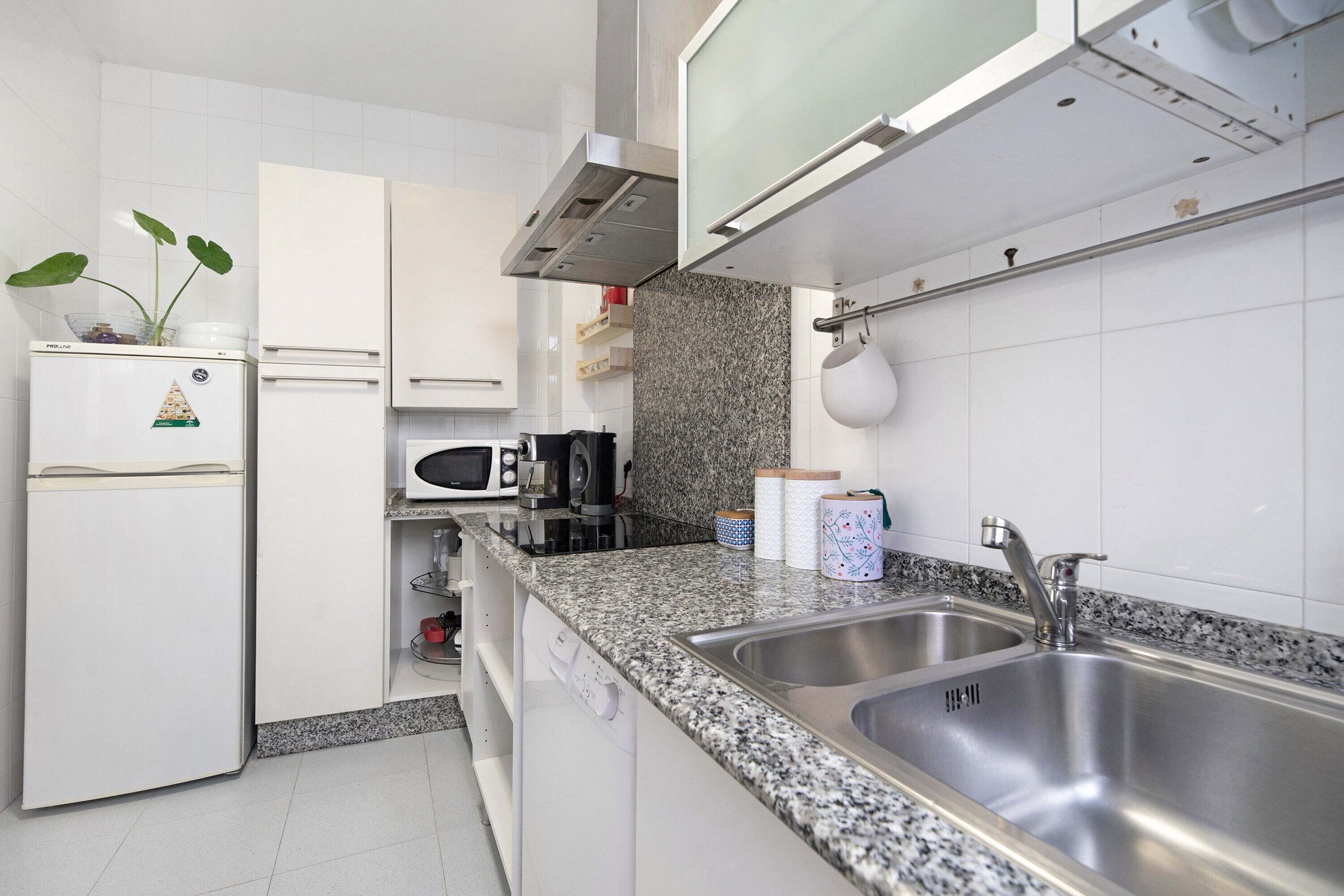 A modern kitchen with white cabinets, a granite countertop, a stainless steel sink, a microwave, and a built-in oven.