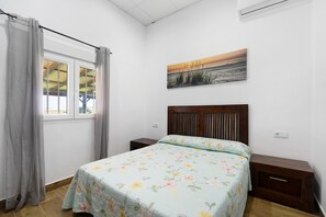 A bedroom with a bed, a nightstand, a window with curtains, and a wall-mounted painting. - Country House 'Villa Pastrana' with Private Terrace, Wi-Fi, and Air Conditioning (Chipiona)