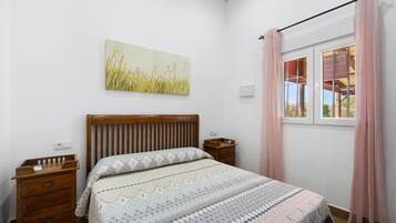 Un dormitorio con cama de madera, mesita de noche, ventana con cortinas y un cuadro colgado en la pared.