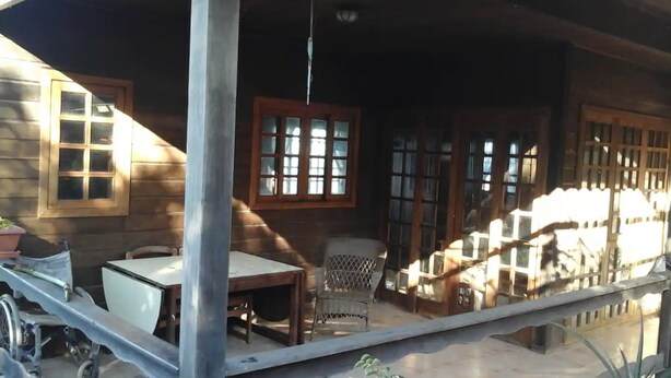 A wooden house with a porch, a table, a chair, and a wheelchair. - Vacation Home 'Chalet Rural Marian' with Sea View, Garden & Wi-Fi (Santa María de Guía)