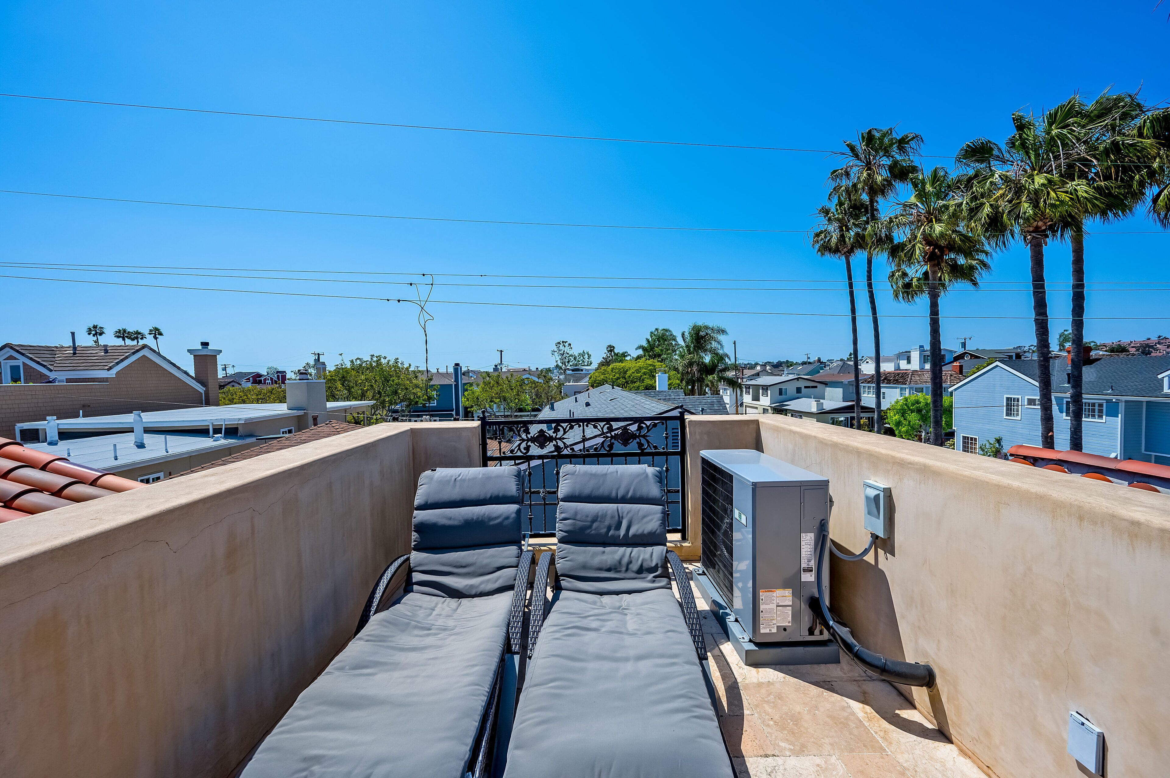 Terraza en la azotea con dos sillones de descanso, un equipo de aire acondicionado y vistas a edificios residenciales y palmeras.