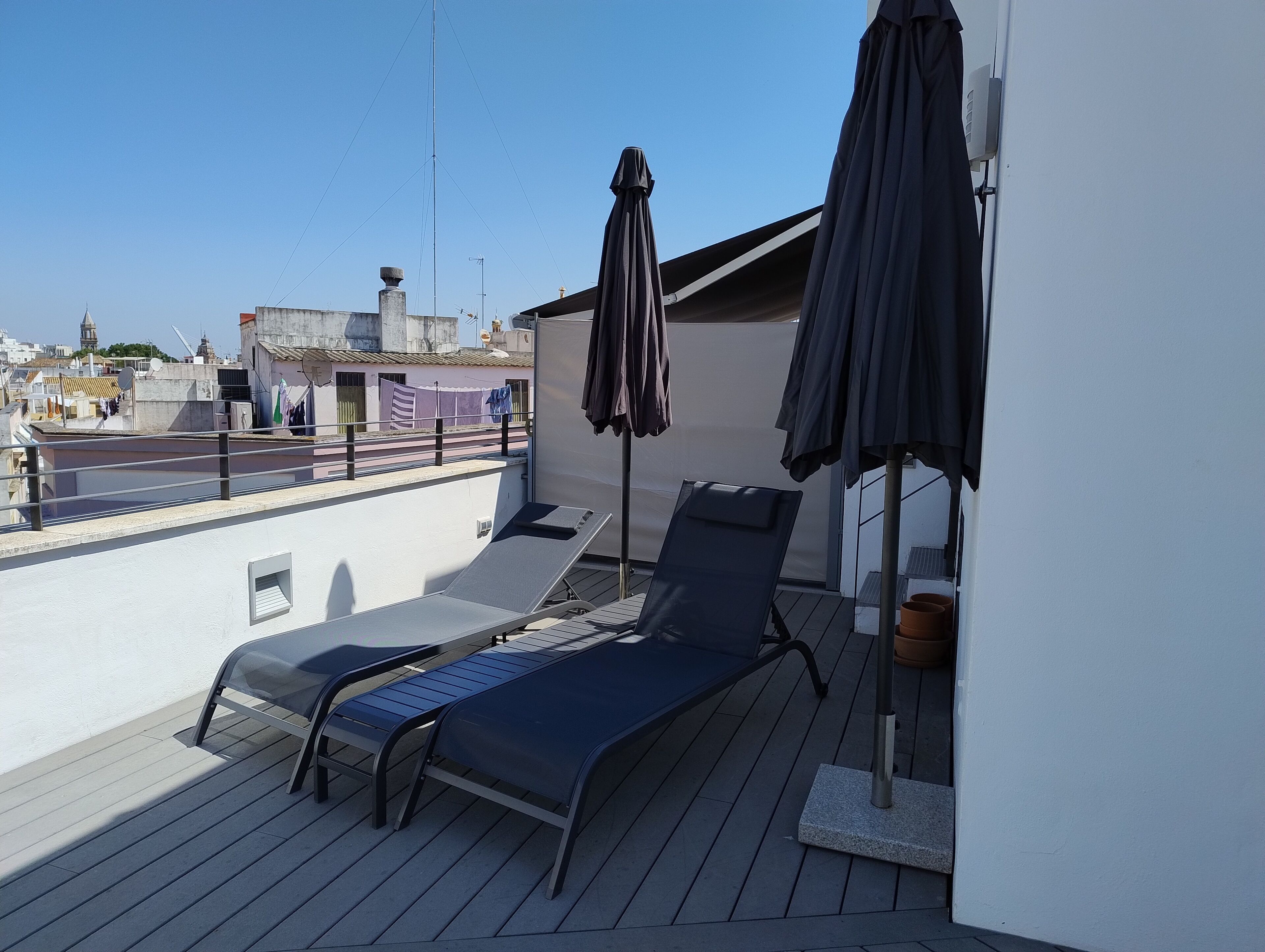 Terraço no telhado com espreguiçadeira, duas guarda-sóis e vista para o horizonte urbano.