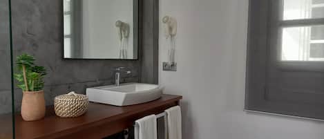 A bathroom with a white sink, a mirror, a hairdryer, a potted plant, and a woven basket on the counter.